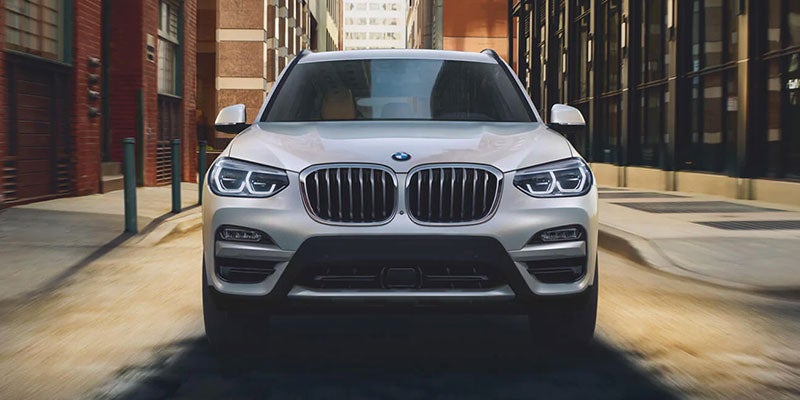 A BMW X3 SUV driving down a city street, with the front view showing its distinctive grille and sleek design