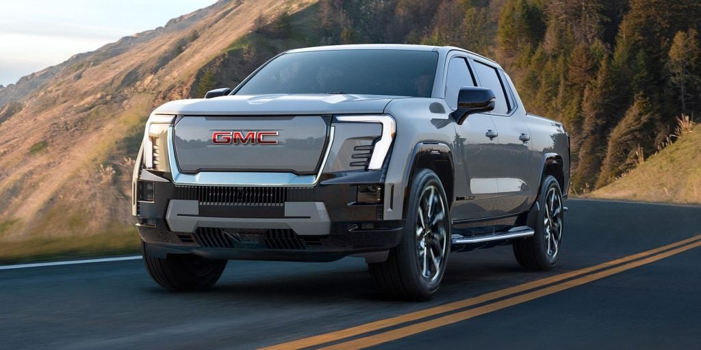 Silver GMC Sierra EV driving on a coastal road.