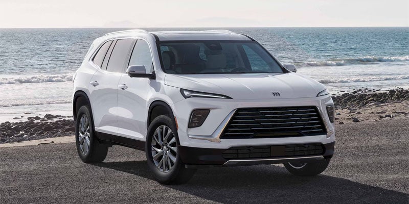 A white Buick Envision SUV parked on an asphalt surface next to a rocky beach with ocean waves in the background.
