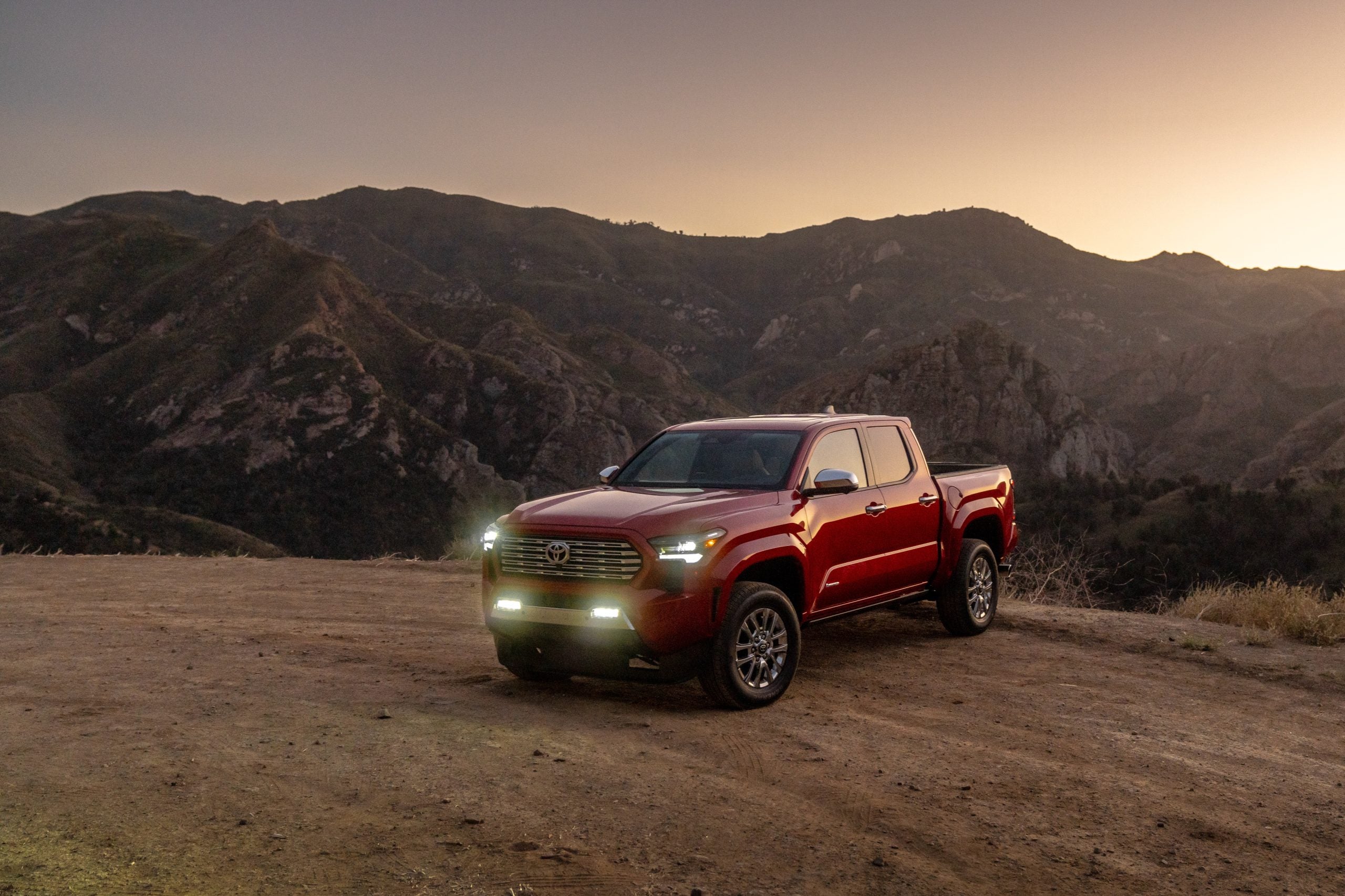 2026 Toyota Tacoma Hybrid in red on a dirt road in front of a mountain view