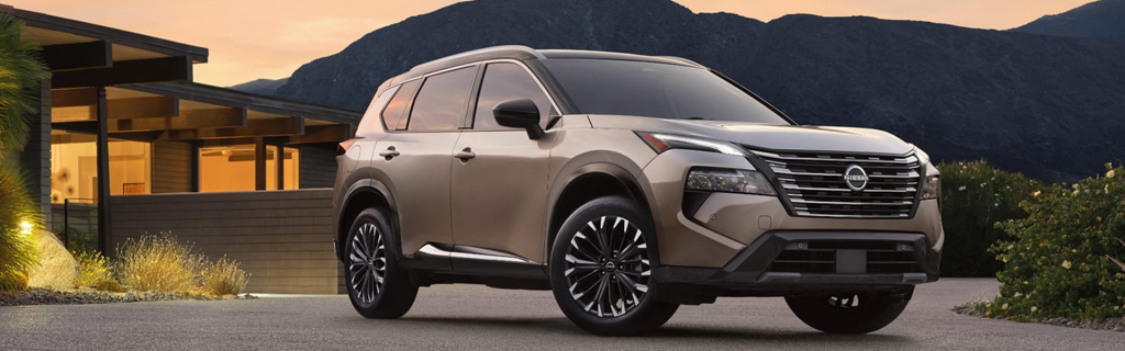 A beige SUV sits in a driveway at sunset beside a modern home with mountains in the background.
