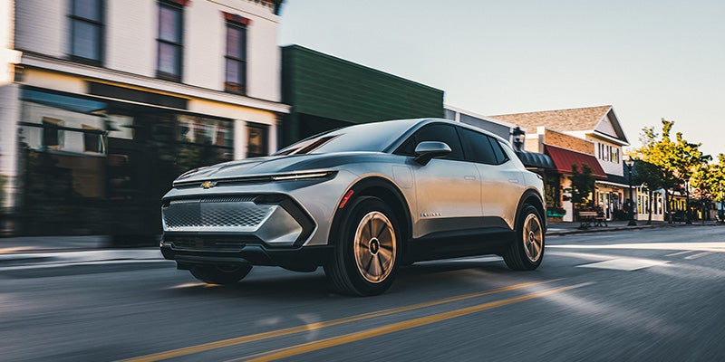 Silver Chevrolet Equinox EV driving down a small-town main street