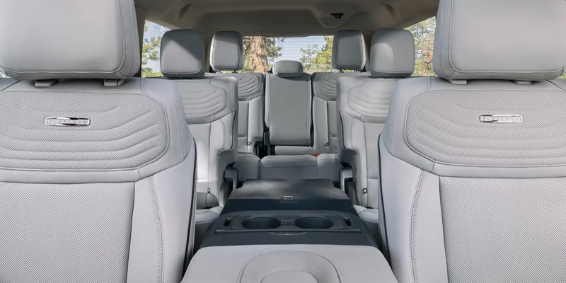 Interior view of a spacious SUV showing three rows of light gray leather seats with foldable armrests and cup holders, highlighting rear passenger comfort and cabin layout.
