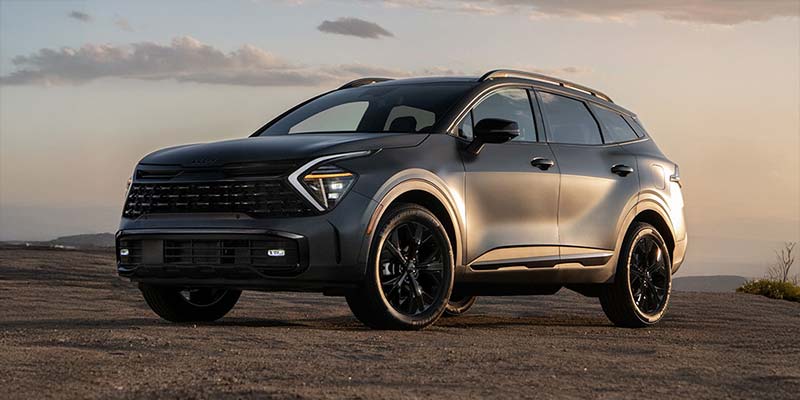 Silver Kia hybrid SUV parked on a scenic overlook during sunset.
