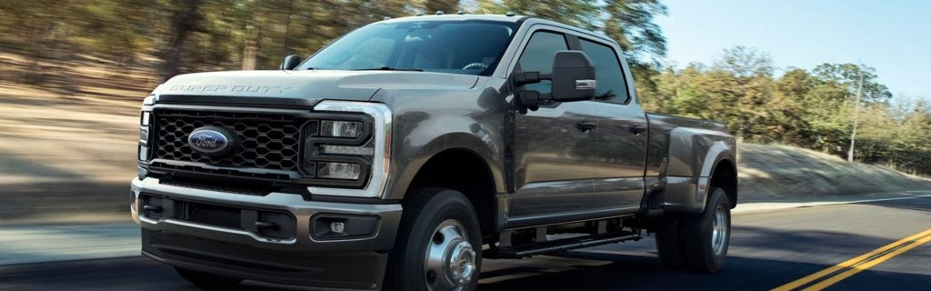 Gray Ford Super Duty pickup truck driving on a road with trees in the background, shown from a front-side angle