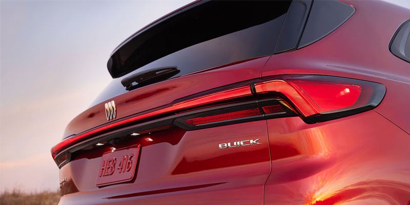 Close-up rear view of a red Buick SUV showing illuminated taillights, Buick badge, and rear liftgate design during sunset.