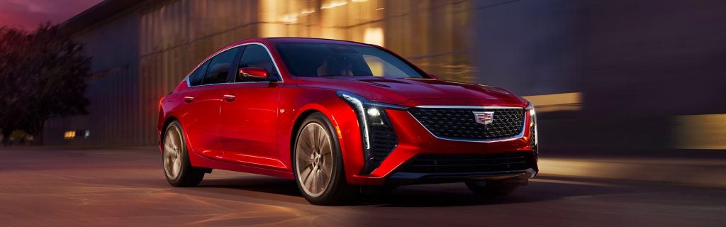 A red Cadillac CT5 sedan parked in a modern urban setting during twilight.