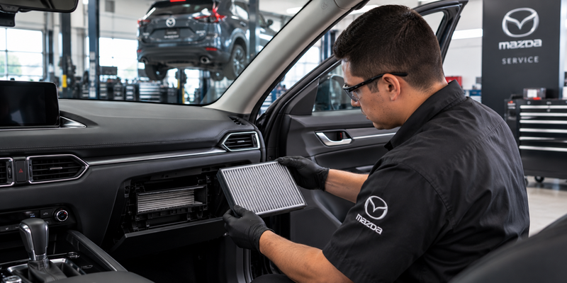 Technician removing a Mazda cabin air filter from the passenger compartment