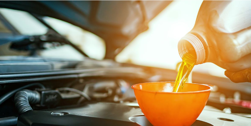 Close-up of motor oil being poured from a bottle into an orange funnel inside a car engine bay during vehicle maintenance.