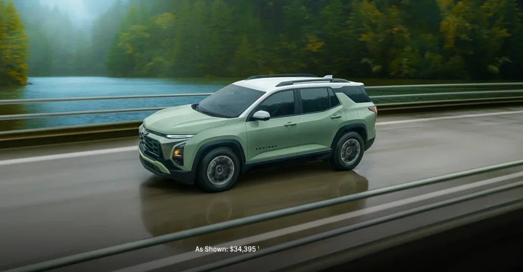 2025 Chevy Equinox in green driving across a scenic bridge over a wide river near Mangino Chevrolet, with wooded hills in the background.