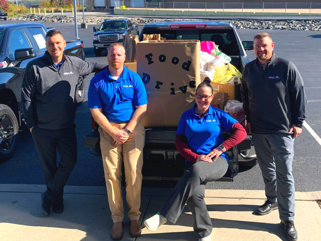 a group of people standing around an open truck bed that has food drive supplies on it. 