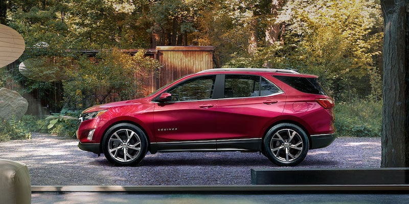 Red Chevrolet Equinox parked outside a wooded home.
