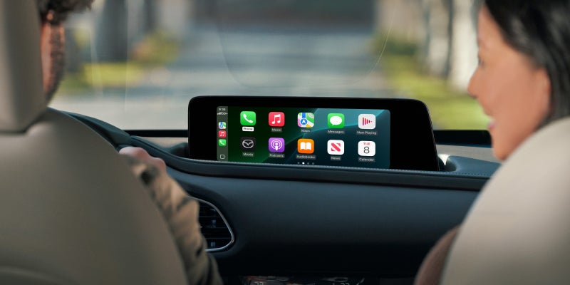 Car dashboard display showing Apple CarPlay interface with apps like Music, Messages, and Maps