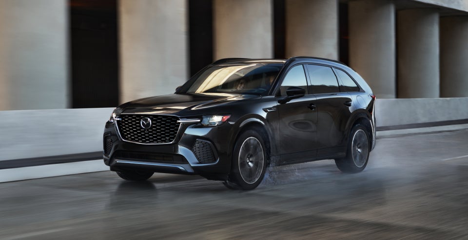 A black Mazda CX-70 SUV driving on a modern urban road