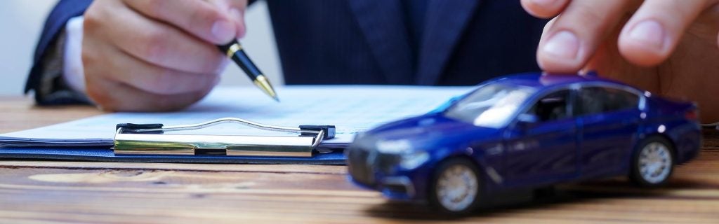 Person reviewing car sale or lease documents with a model car on desk
