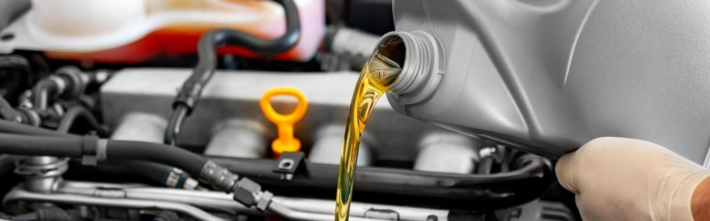 A hand pouring motor oil into a car engine with the oil dipstick visible in the background