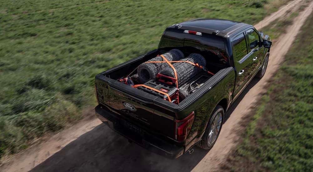 Ford%20F-150%20for%20Sale%202024%20Ford%20F-150%20-%20Black%20Driving%20Above.jpg A black 2024 Ford F-150 driving on a dirt road with supplies in the bed.