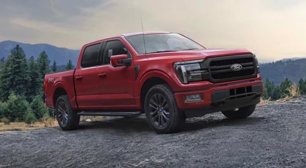 Used Truck Dealer - 2024 Ford F-150 Lariat - Trees.jpg A red 2024 Ford F-150 Lariat is shown parked off-road after visiting a used truck dealer.