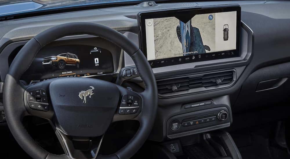 Ford%20Bronco%20Sport%20for%20sale%20near%20Newburgh%202025%20Ford%20Bronco%20Sport%20-%20Infotainment.jpg A person is putting gear in the under seat storage in a 2025 Ford Bronco Sport Badlands.