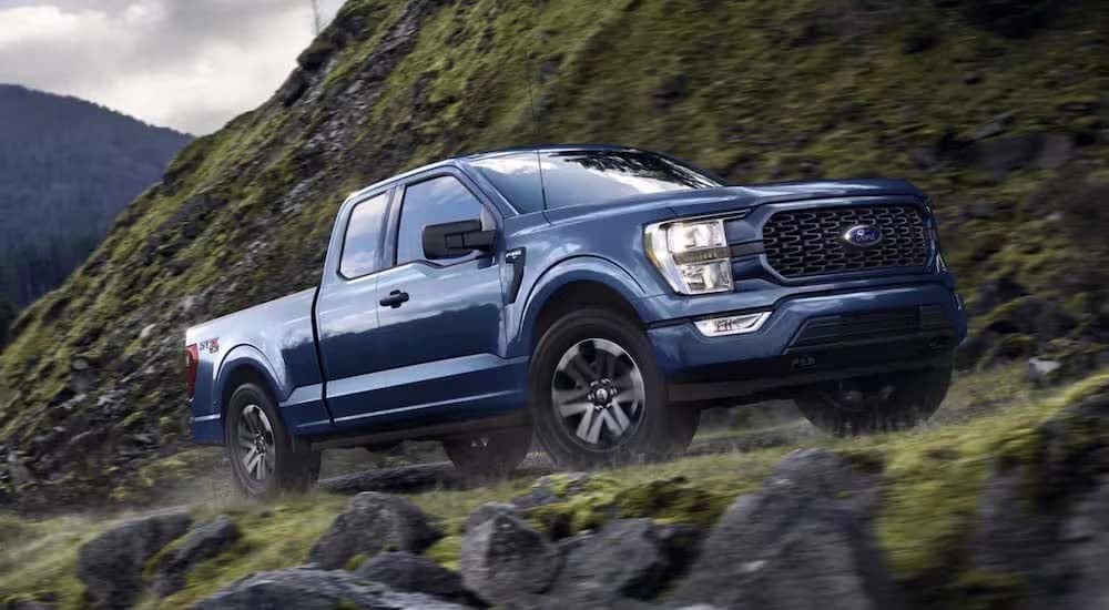 A blue 2022 Ford F-150 STX is shown from the side driving on a mountain road.