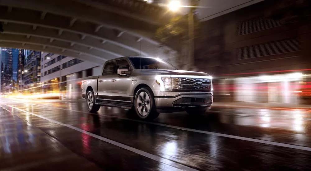 A silver 2022 Ford F-150 Lightning Platinum is shown driving though a city after leaving a Owensboro…
