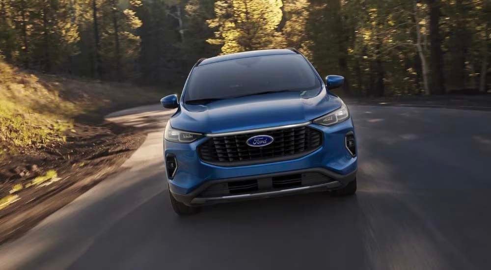 A blue 2023 Ford Escape for sale is shown driving on a tree-lined road.