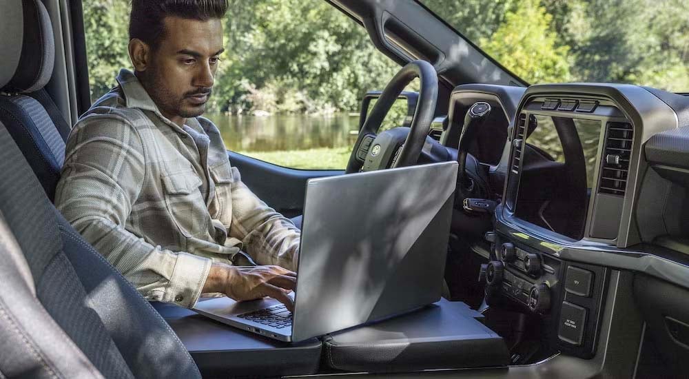 A man using a laptop in a 2025 Ford F-150 at a Ford dealer near Ownesboro.