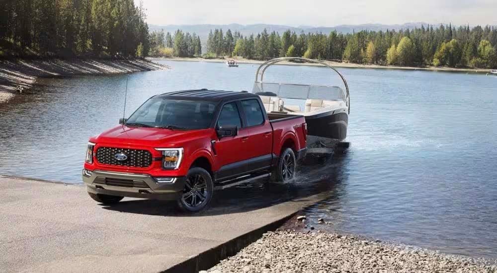 A red 2023 Ford F-150 XLT Heritage Edition is shown towing a boat near a lake.