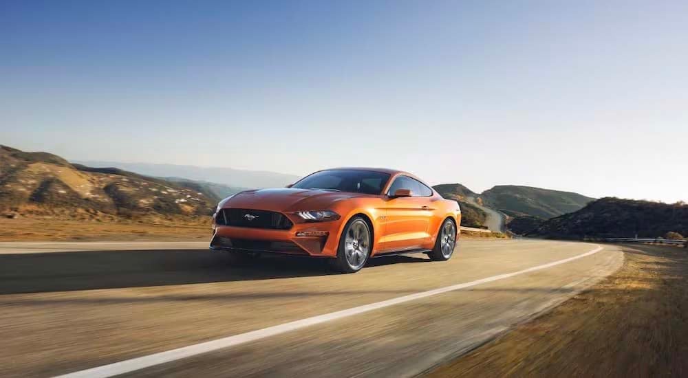 An orange 2018 Ford Mustang GT is shown driving on an open road.