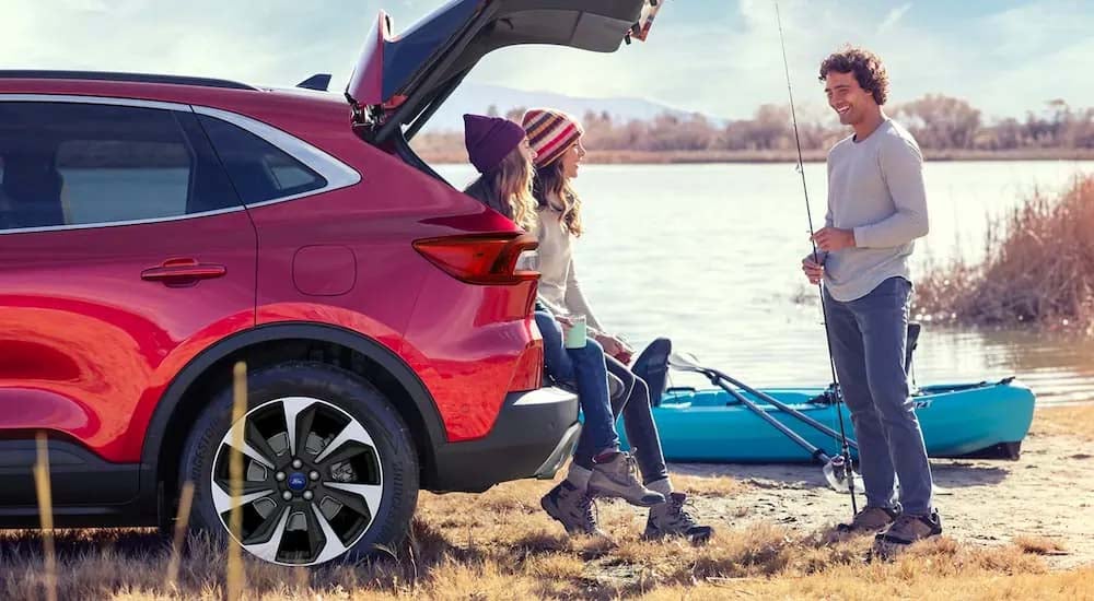 People are shown sitting in the trunks of a red 2023 Ford Escape next to a lake.
