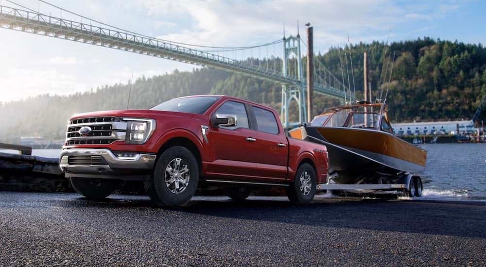 A red 2022 Ford F-150 is shown towing a boat after leaving a Ford truck dealership.