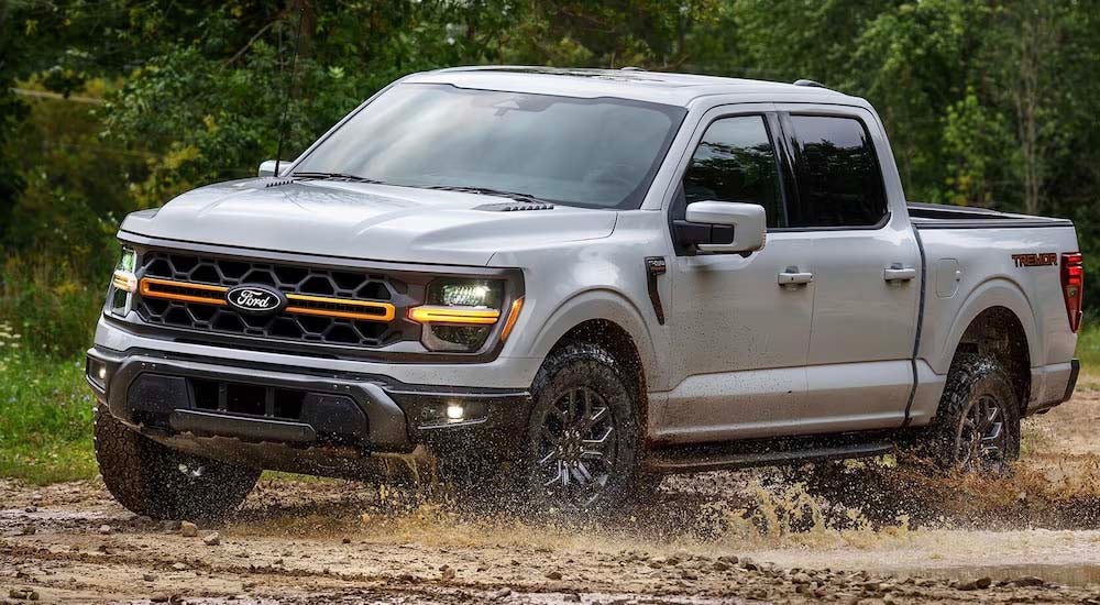 A grey 2025 Ford F-150 Tremor splashing through a muddy puddle.