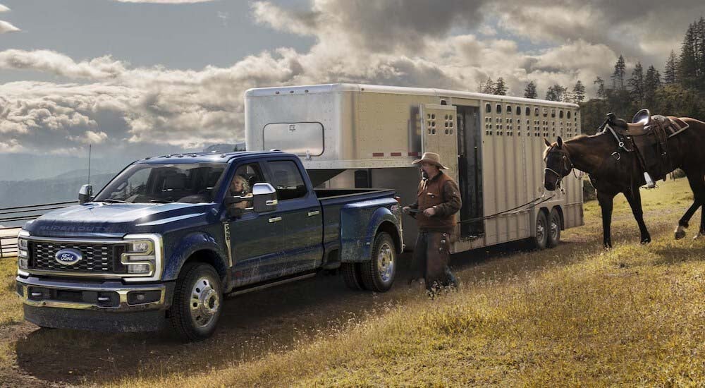 A blue 2024 Ford F-450 Super Duty is shown towing a horse trailer.