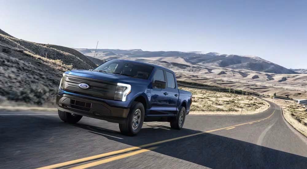 A blue 2022 Ford F-150 Lightning Pro is shown driving on an empty road.
