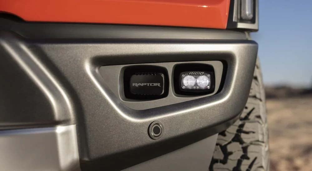 A close up shows the bumper light on an orange Ford F-150 Raptor.