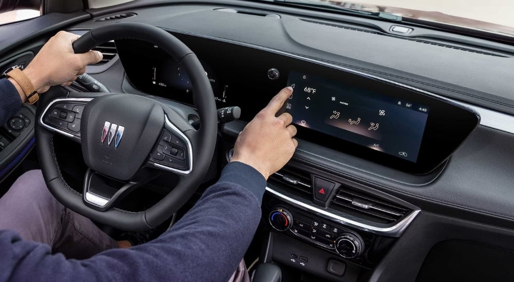 A close-up shows a person using the infotainment screen in a 2025 Buick Encore GX.