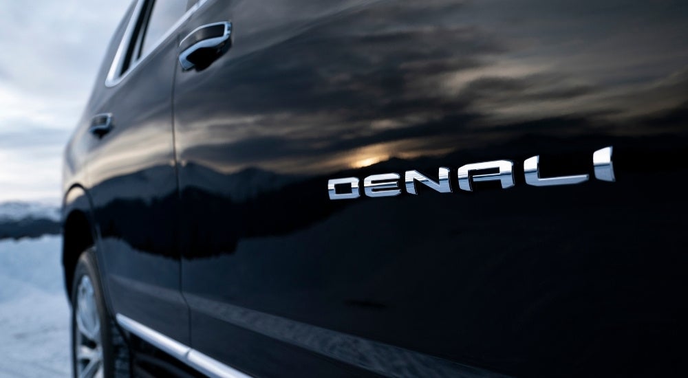 A close-up shows the Denali badge on a black 2023 GMC Yukon Denali .