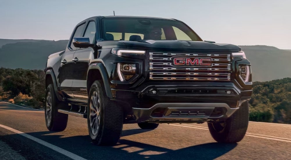 One of the most popular trucks for sale near Minneapolis, a black 2024 GMC Canyon Denali, is shown driving on an open road.