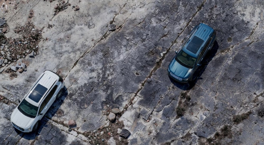 A white and a blue 2024 GMC Acadia for sale are shown from above parked on rocks.