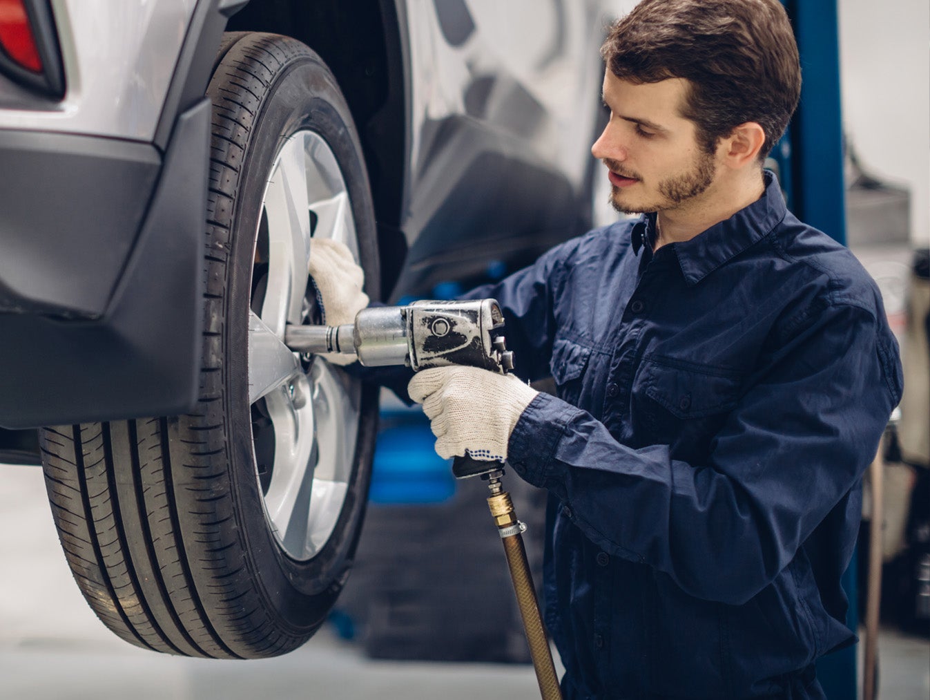 Mechanic using an impact wrench to change a car tire on a lift.