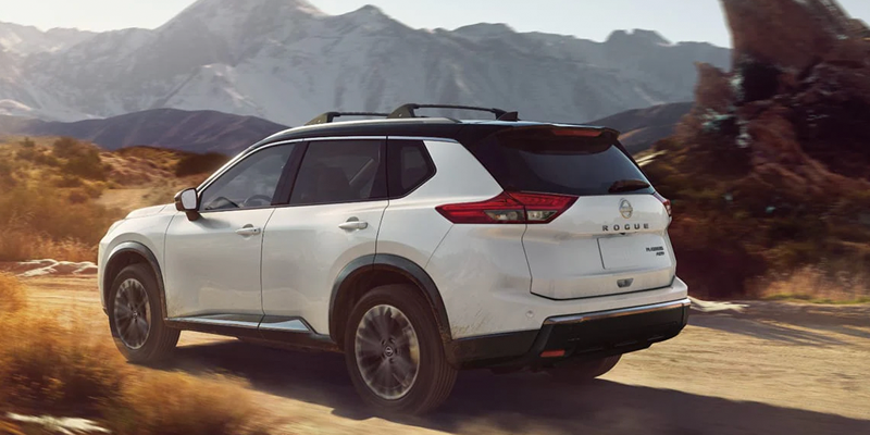 White Nissan Rogue driving on a desert dirt path.