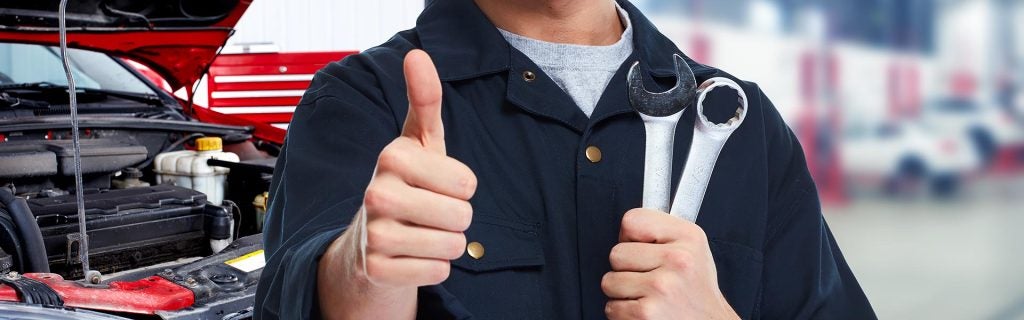 Auto service technician holding wrenches thumbs up
