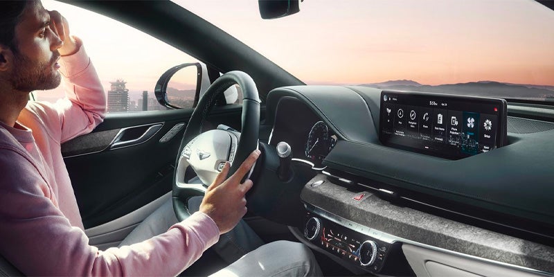 Driver inside a modern car using digital dashboard and infotainment system at sunset.