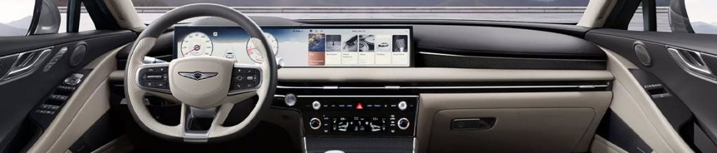 Interior view of a Genesis G80, showing the steering wheel, digital instrument cluster, and wide infotainment touchscreen across the dashboard.