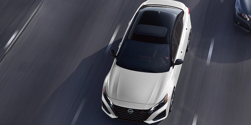 White Nissan Altima with a black roof driving on a highway