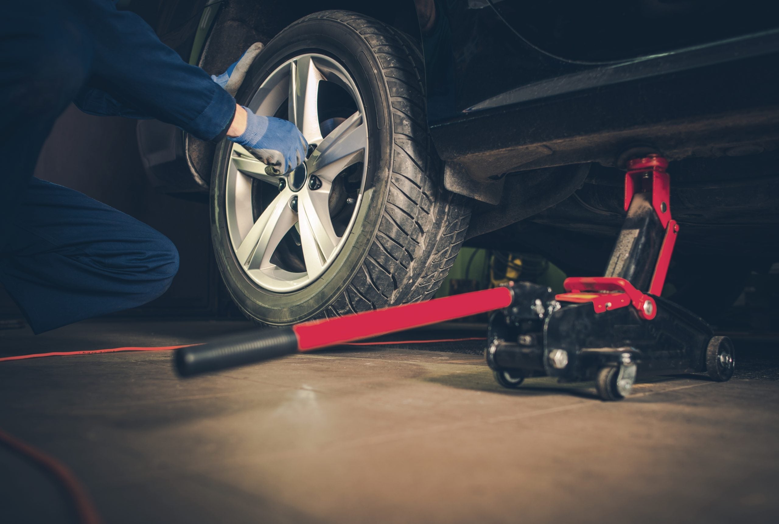 A mechanic using a jack to lift a car while removing a wheel.