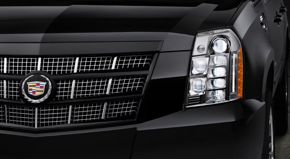 A close-up shows the driver side headlight on a black 2014 Cadillac Escalade.