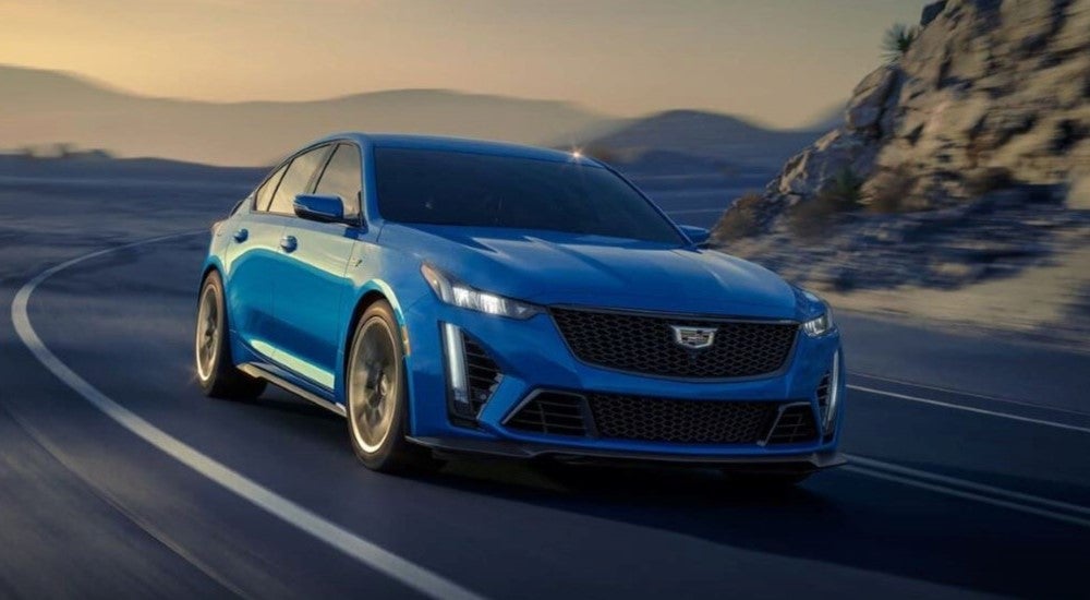 A blue 2024 Cadillac CT5-V Blackwing is shown rounding a corner after leaving a Cadillac dealer near Rochester.