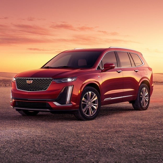 Red luxury 2026 Cadillac XT6 SUV parked on a desert road at sunset, featuring a bold chrome grille, LED vertical headlights, and sleek modern design.