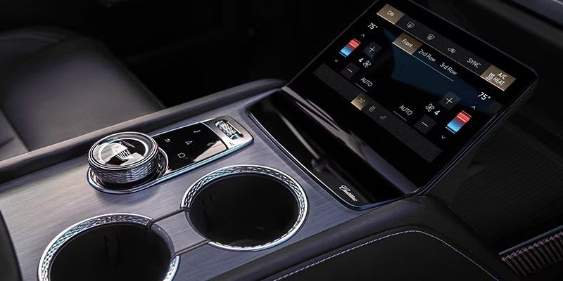 Cadillac center console with touchscreen climate controls, cupholders, and rotary dial.